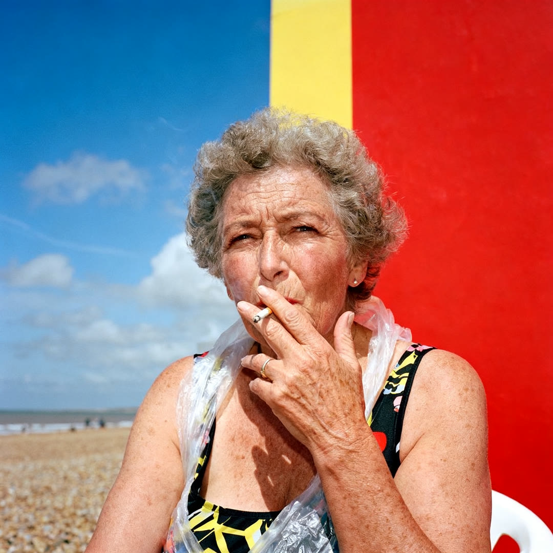 AI-generiertes Editorial: rauchende Frau vor rot-gelber Wand am Strand